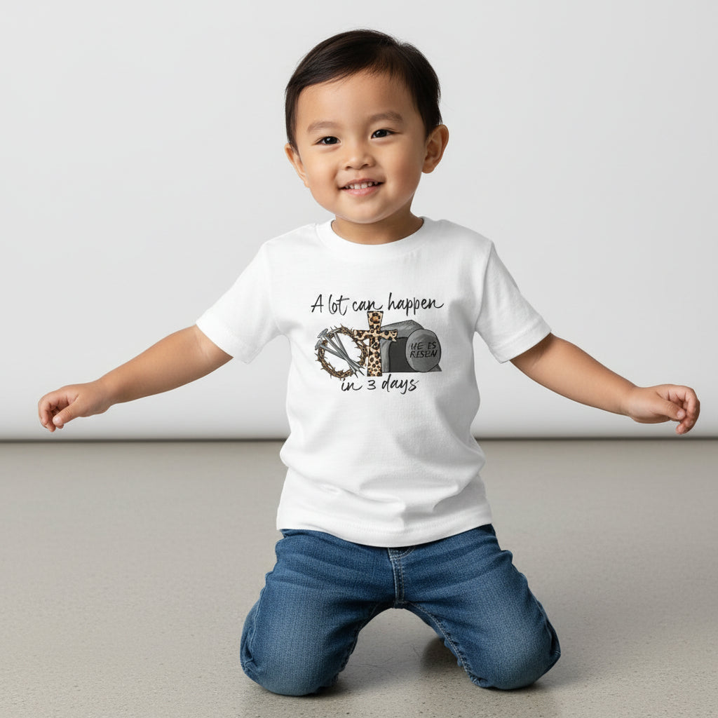 Child wearing a white t-shirt with a graphic and text, sitting on the floor against a plain background