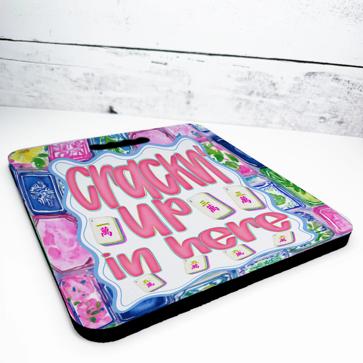 Colorful seat cushion with text 'Crackin' Up in Here' on a white wooden surface