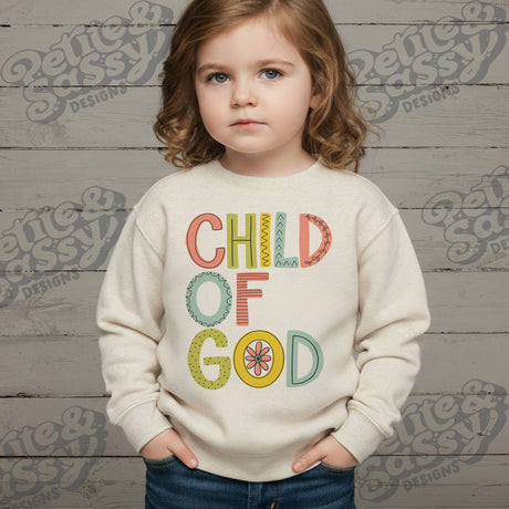 Child wearing a sweatshirt with 'Child of God' text in front of a wooden background with 'Petite & Posh Designs' branding.