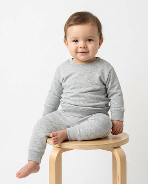 A baby wearing a light gray heathered long-sleeve top and matching pants, sitting on a light wood stool against a plain white background.