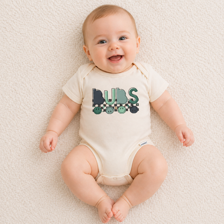 Baby wearing a onesie with 'BUBS' printed on it, sitting on a soft surface.
