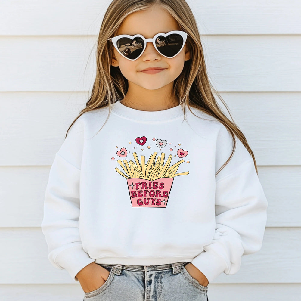 A child wearing a white sweatshirt with a graphic design of fries before guys, standing against a light-colored wall.