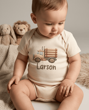 A baby sitting and wearing a cream-colored ribbed bodysuit with a graphic of a truck carrying logs and the name 'Larson' printed below. The background features a soft gray wall and plush stuffed toys.