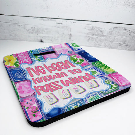 Colorful seat cushion with I've been known to pass wind, " mahjong-themed text, and decorative elements on a wooden surface